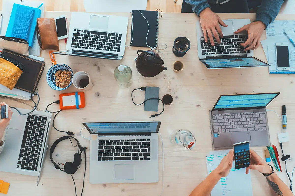 An overhead view of a team working on laptops, representing an agency scaling its AI services to sell online.