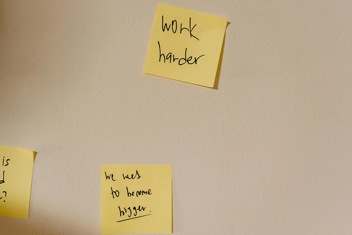 Sticky notes on a wall with motivational phrases like 'work harder,' illustrating strategies on how to start the new year with consistent effort.
